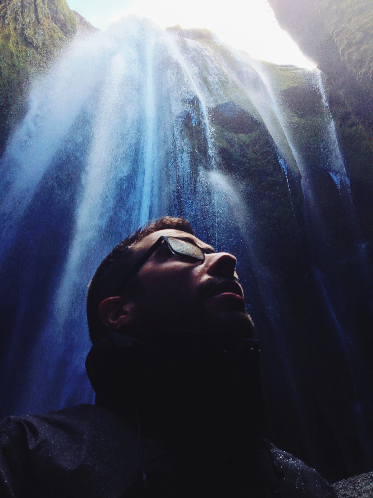 Alberto standing at the base of Gljúfrabúi waterfall in Iceland, looking up as water cascades down the cliffs above.